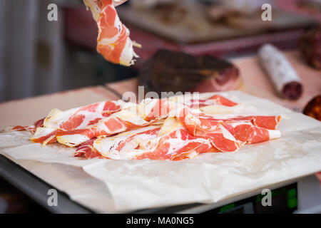 Nahaufnahme der dünne Scheiben Prosciutto Crudo, italienischer Schinken Gewicht auf die Waage im Lebensmittelgeschäft. Realen Szene im Supermarkt, Store organische Produkte Stockfoto