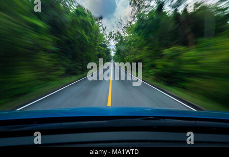 Vorderansicht des blaues Auto Fahren mit hoher Geschwindigkeit in der Mitte der asphaltierten Straße mit weißen und gelben Linie des Verkehrs-Symbol in den grünen Wald. Bäume b Stockfoto