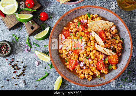 Chili con Carne der Türkei mit Kichererbsen, serviert mit Nachos. Chili mit Fleisch, Nachos, Kalk, Paprika. Mexikanische/Texas traditionelles Essen. Ansicht von oben Stockfoto