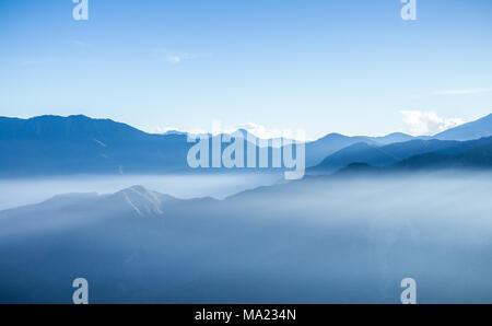 Dunstig blauen Berge von Zhushan in Alishan Erholungsgebiet in Taiwan durch Nebel bei Sonnenaufgang am Morgen bedeckt mit hellen Himmel. Stockfoto