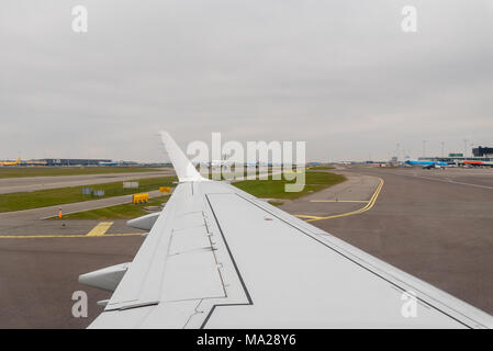 Eine Ansicht aus einem landete Verkehrsflugzeug Rollen entlang einer Start- und Landebahn am Queue von aufgereiht Flugzeuge auf dem Flughafen Amsterdam Schiphol, Niederlande suchen. Stockfoto