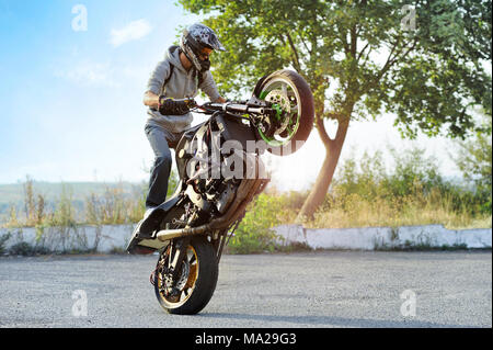 Ternopil, Ukraine - 28. August 2015: junge Biker das Tragen schützender helm ist maiking Tricks auf Sommer zitieren Straße. Grüne Bäume und Pflanzen, blauen Himmel im Hintergrund. Stockfoto