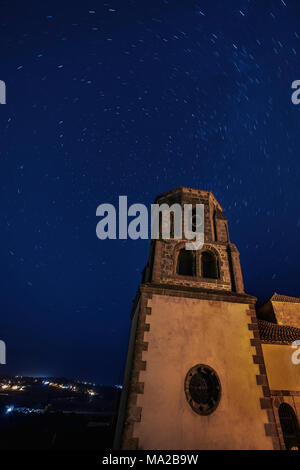 Übersicht Star trails wirbelnden im Himmel über Turm der Kirche und ein Dorf im Hintergrund beleuchtet Stockfoto