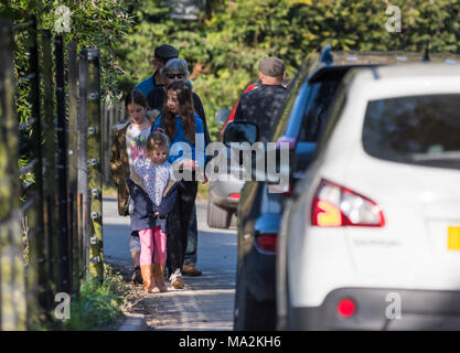 Leute, die einzelne Datei Vergangenheit Autos entlang einer schmalen Straße ohne Bürgersteig in Großbritannien. Stockfoto