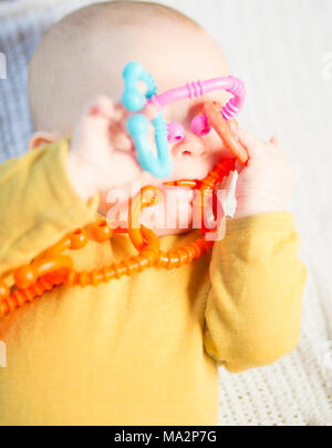 Sehr niedliches Baby Junge spielt mit Ring der O'links Spielzeug, die bedeckte sein Gesicht rattle Stockfoto