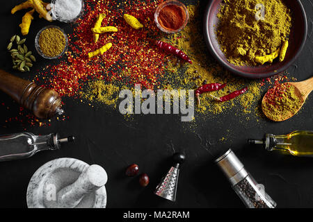 Kochen mit frischen Gewürze mit Mörtel und kleine Schalen von Spice auf einem Schwarzen Tisch mit Pulver verschütten auf seiner Oberfläche, Ansicht von oben mit copysp Stockfoto