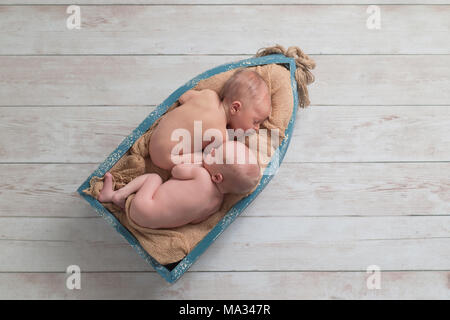 Sechs Tage alten Zwillingsbruder, Neugeborenes, Baby jungen schlafen in einem kleinen, hölzernen Boot. Gedreht im Studio auf einem hölzernen Hintergrund. Stockfoto