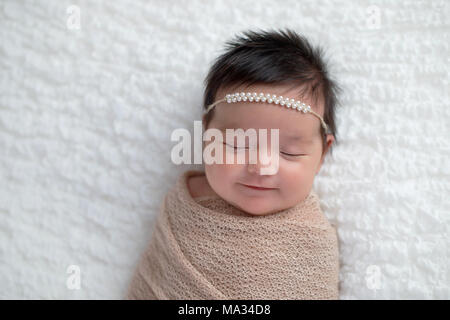 Lächelnd einen Monat altes Baby girl Gepuckte in Beige wickeln. Im Studio auf einer weißen Decke geschossen. Stockfoto