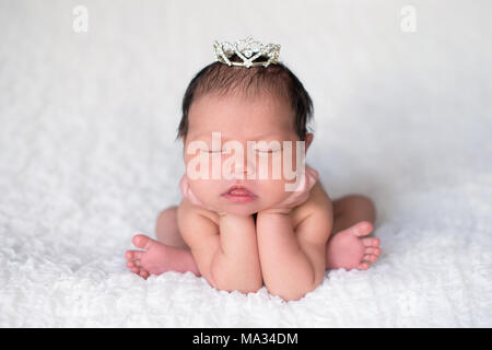 Portrait von sieben Tage alten Schlafen neugeborene Mädchen. Sie trägt ein Strass Krone und ist mit ihr Kinn auf ihre hände aufgeworfen. Stockfoto