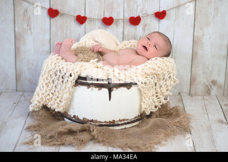Lächelnd sechs Wochen altes Baby boy in einem hölzernen Löffel mit Herz Girlande liegen. Im Studio auf einem Holz Hintergrund gedreht. Stockfoto