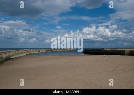 Strand-Szene im Seaham Harbour in County Durham mit Strand, der von lockenden Piers und spielenden Kindern umgeben ist