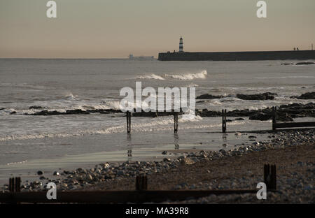 Eingang zum Hafen von Seaham am am frühen Abend mit Leuchtturm und Schiff im Hintergrund und Strand und alten Meeresgroschen im Vordergrund Stockfoto