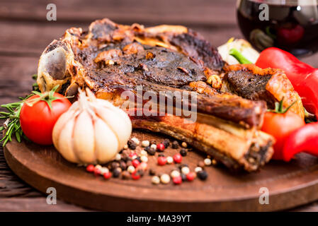 Close up lecker Gegrilltes Beefsteak mit Pfeffer, Knoblauch, Tomaten und Paprika auf dunklem Hintergrund und ein Glas Wein. Selektiver Fokus Stockfoto