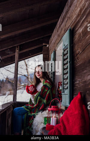 Junge Frau, in eine Decke eingewickelt auf dem Balkon zu sitzen und Halten einer Tasse Stockfoto