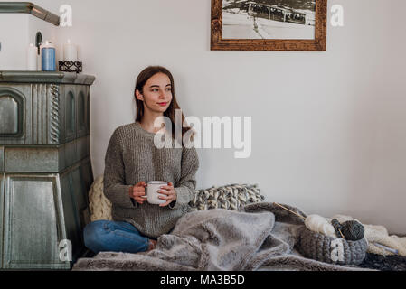 Junge Frau sitzt neben einem Kachelofen und Getränke Kaffee Stockfoto