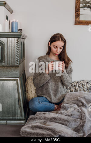 Junge Frau sitzt neben einem Kachelofen und Getränke Kaffee Stockfoto