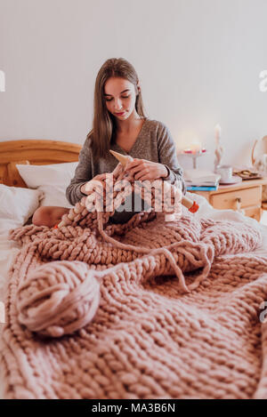 Junge Frau im Bett sitzen und stricken mit XXL Wolle Stockfoto