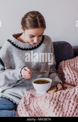 Junge Frau sitzt auf einem Sofa und Essen eine Suppe Stockfoto