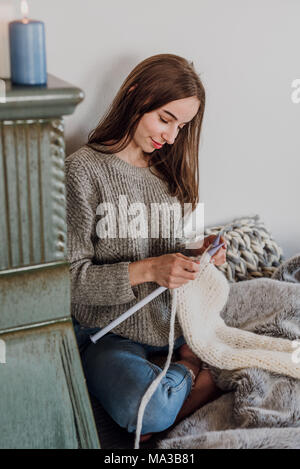 Junge Frau sitzt neben einem Kachelofen und strickt Stockfoto