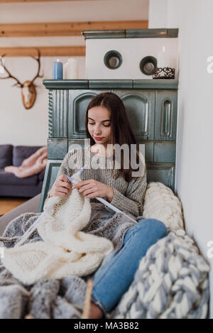 Junge Frau sitzt neben einem Kachelofen und strickt, detail, Stockfoto