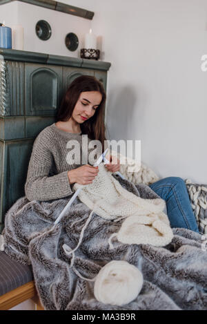 Junge Frau sitzt neben einem Kachelofen und strickt, detail, Stockfoto