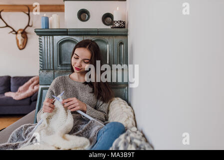 Junge Frau sitzt neben einem Kachelofen und strickt, detail, Stockfoto