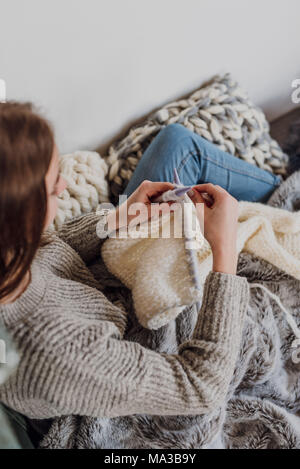 Junge Frau sitzt neben einem Kachelofen und strickt, detail, Stockfoto
