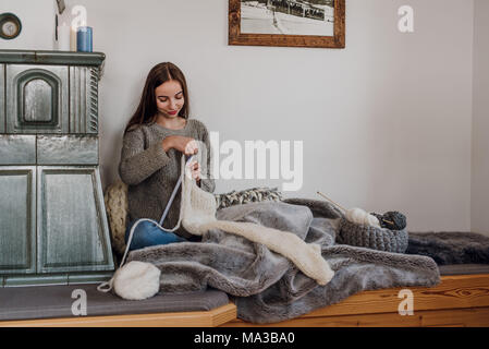 Junge Frau sitzt neben einem Kachelofen und strickt Stockfoto