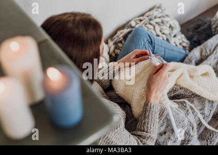 Junge Frau sitzt neben einem Kachelofen und strickt, Detail, Kerzen, Blur, Stockfoto