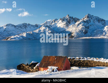 Blue Sky auf den Hütten genannt Rorbu umrahmt von gefrorenen Meer und schneebedeckten Gipfeln Stockfoto