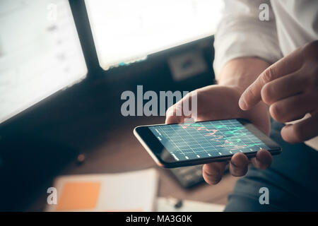 Mann hält Telefon in der Hand und prüft Verkaufscharts. Innen-, Studio gedreht. Arbeiten, Business, Handel Konzept Stockfoto