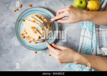 Hausgemachte Frühstück: amerikanische Pfannkuchen serviert mit Beeren, Birnen und Honig auf konkreten Hintergrund. Frau Hände, Pfannkuchen, Ansicht von oben Stockfoto