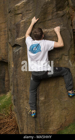 Junger Mann Klettern (Bouldern) ohne Seile auf bräunliche Rock. Stockfoto