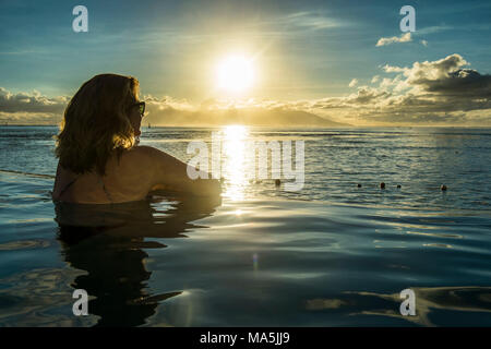 Frau genießen den Sonnenuntergang in einem Schwimmbad mit Moorea im Hintergrund, Papeete, Tahiti, Französisch-Polynesien Stockfoto