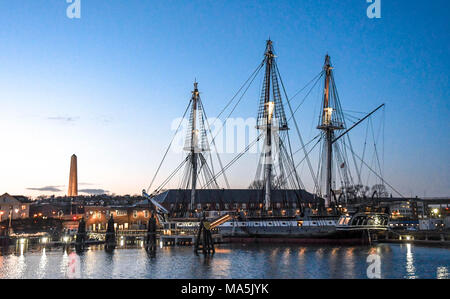 Die U.S.S. Verfassung, die in der Amerikanischen Revolution kämpfte, im Hafen von Boston mit dem Bunker Hill Monument im Hintergrund angedockt bei Sonnenuntergang. Stockfoto