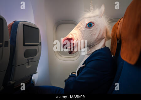 Seltsame junge Mann in lustige Maske reist mit dem Flugzeug. Ungewöhnliche Passagier im eleganten Anzug sitzt alleine im Flugzeug und Flug weg bereit. Stockfoto