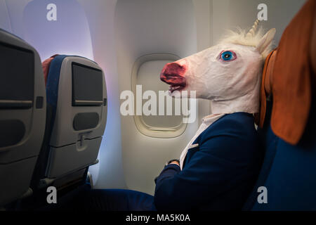 Ungewöhnliche Passagier im eleganten Anzug sitzt alleine im Flugzeug und bereit zur Abreise. Junger Mann in lustige Maske Reisen mit dem Flugzeug Stockfoto