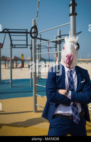 Ungewöhnliche Fitness Trainer in Anzug und Maske begrüßt Sie am Sportplatz in der Nähe von Strand. Seltsamer Mann bereit, die Muskeln zu pumpen. Einhorn Fitness im Freien Stockfoto