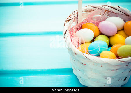 Ostern bunte Eier in süßen weißen Stroh Korb auf Türkis Holz- Hintergrund. Copyspace Stockfoto
