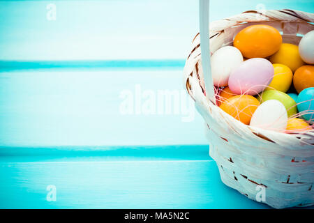 Ostern bunten Süßigkeiten Eier in Weiß Stroh Korb auf Türkis Holz- Hintergrund. Copyspace Stockfoto