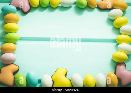 Frohe Ostern. Bunten Süßigkeiten Süße Eiern und Schokolade Kaninchen auf Blau Holz- Hintergrund. Rahmen. Ansicht von oben. Copyspace Stockfoto