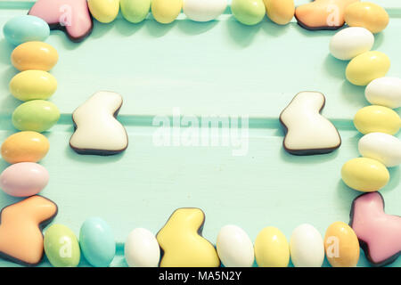 Frohe Ostern. Pastellfarben süßen Eiern und Schokolade Kaninchen auf Minze Holz- Hintergrund. Framing. Ansicht von oben. Copyspace Stockfoto