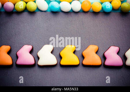 Ostern bunte süße Kaninchen in einer Reihe mit kleinen Süßigkeiten Eier auf schiefer Schneidbrett Hintergrund. Ansicht von oben. Copyspace Stockfoto