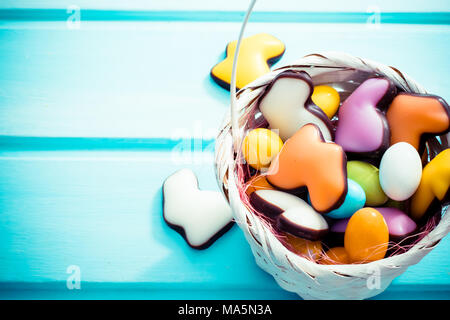 Frohe Ostern. Weiße Stroh klein Korb voller bunte Süßigkeiten Eiern und Schokolade Kaninchen auf hellblauem Hintergrund. Copyspace. Ansicht von oben. Stockfoto
