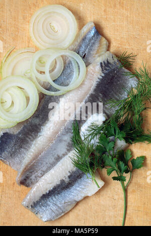 Heringe mit Zwiebeln in Scheiben geschnitten und Grüns auf Holz- Hintergrund Stockfoto