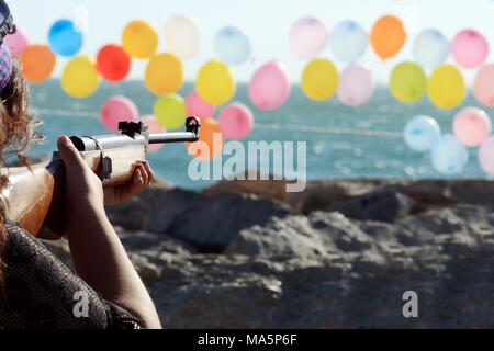 Frauen schießen eine Waffe für farbige Ballons auf Hintergrund mit Meerblick Stockfoto