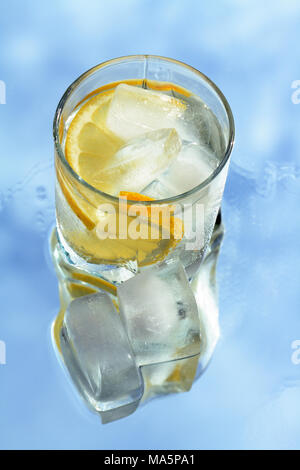 Glas Wasser mit in Scheiben geschnittenen Zitrone und Eiswürfel auf blauem Hintergrund Stockfoto