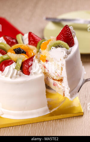 Anheben einer Scheibe des weißen Kuchen gekrönt mit frischem Obst. Stockfoto