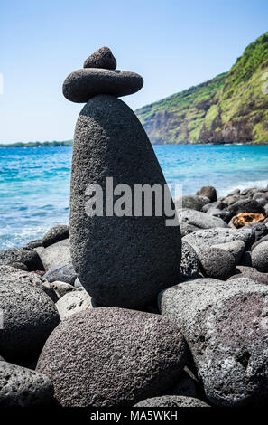 Ein Felsen Cairn auf einem felsigen Strand mit Kealakekua Bay im Hintergrund und Captain Cook Memorial auf der gegenüberliegenden Seite der Bucht. California, South Kona. Stockfoto