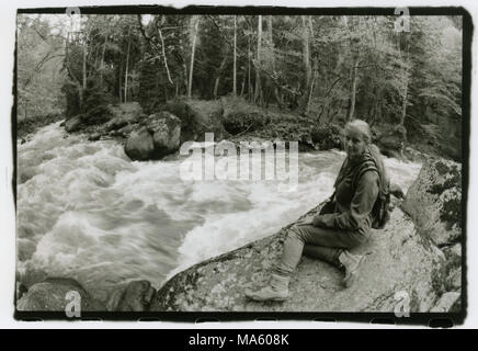 Ein Mädchen mit einem Rucksack auf dem Rücken sitzt am Ufer. Achtung! Das Bild enthält Granularität und andere Artefakte der analogen Fotografie! Stockfoto